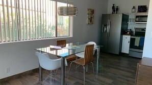 A modern kitchen with a glass dining table, wooden chairs, and a stainless steel refrigerator.