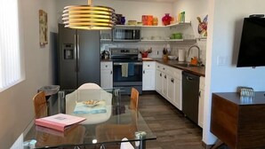 A modern kitchen with white cabinets, a microwave, and a stove. There is a dining table with chairs and a glass top.
