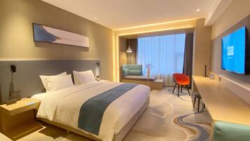 A modern hotel room with a large bed, a desk, a chair, and a TV on the wall.