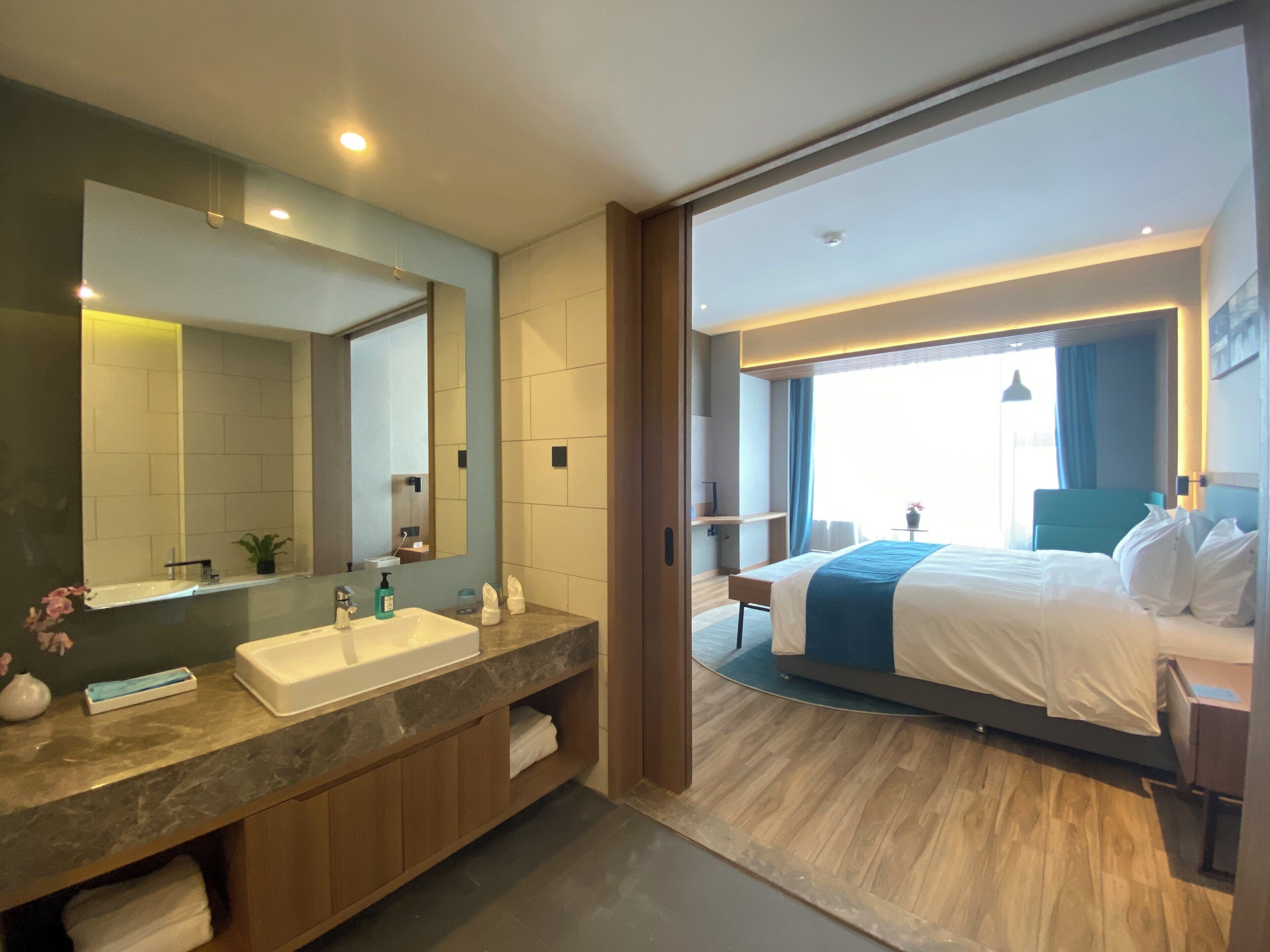 A modern hotel room with a bathroom, a bed, and a view of the outdoors.
