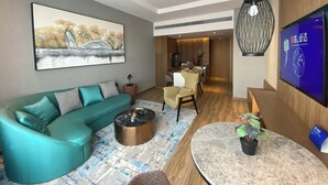 A modern living room with a teal sofa, a coffee table, a flat-screen TV, and a dining area with a wooden table and chairs. - Holiday Inn Express Liaocheng Chiping by IHG (Liaocheng)