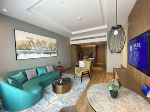 Un salon moderne avec un canapé de couleur turquoise, une table basse, un téléviseur à écran plat et un coin repas comprenant une table et des chaises en bois.