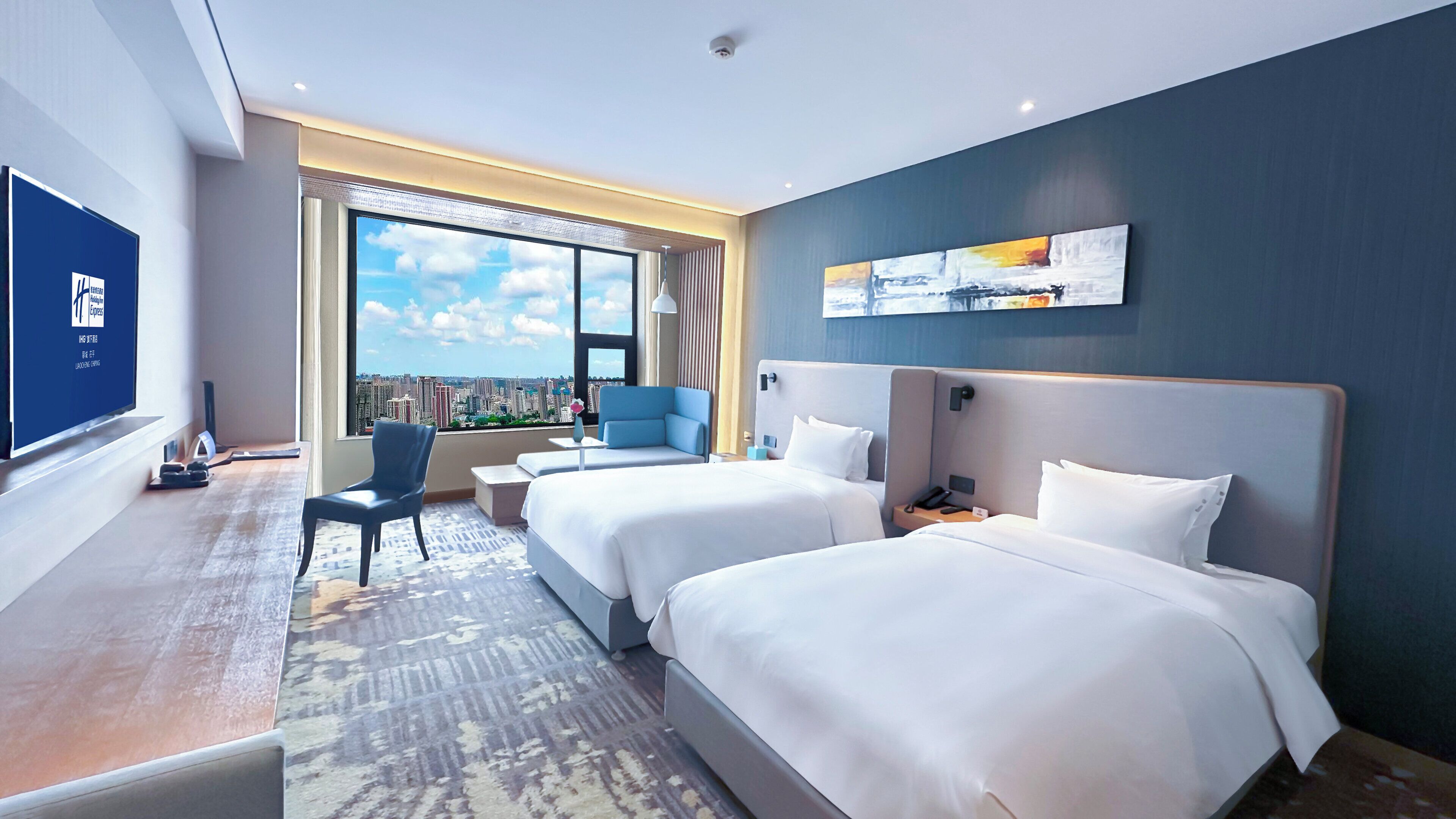 A hotel room with two beds, a desk, a chair, and a large window offering a city view.