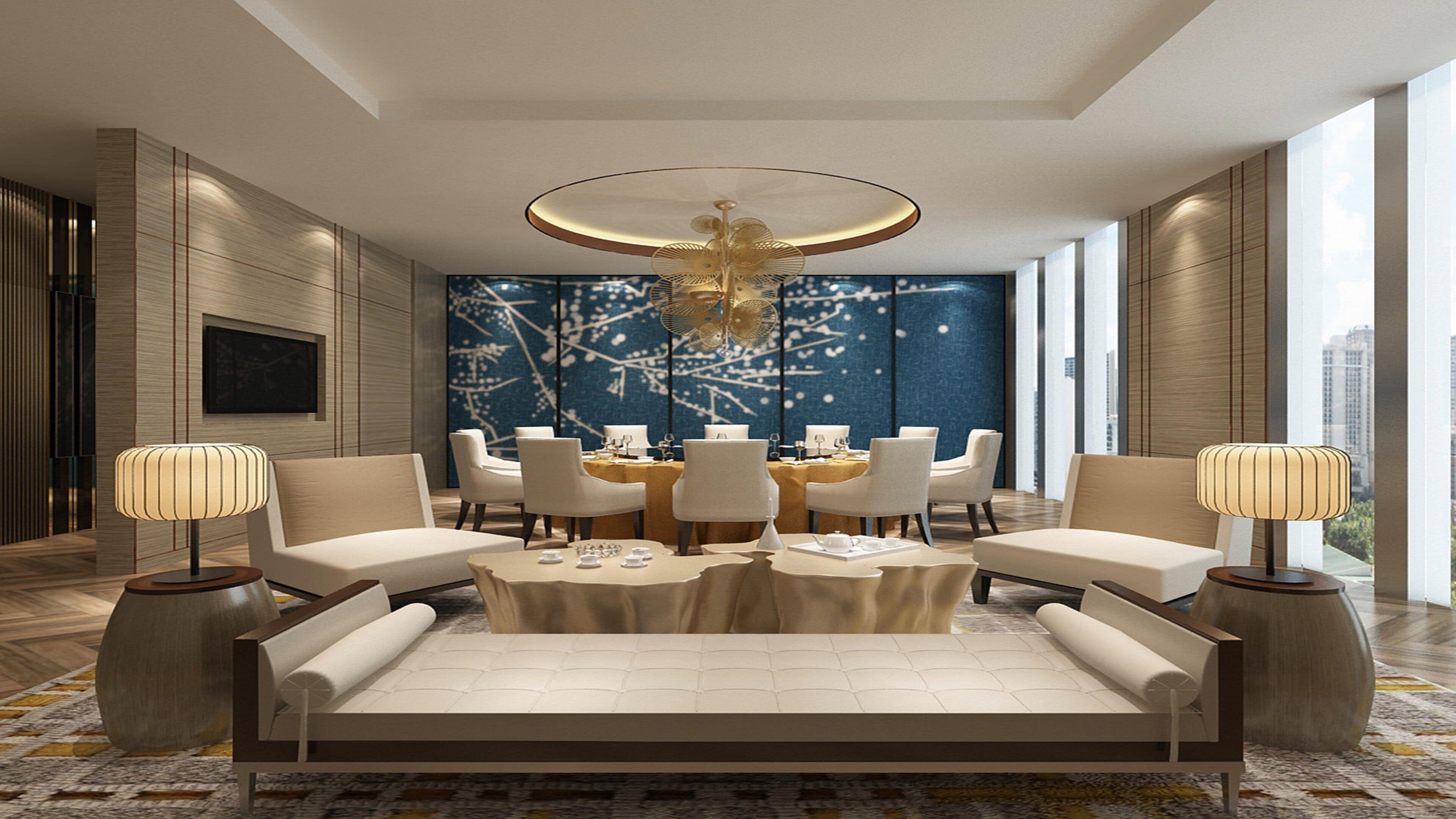 A modern hotel room with a large sofa, dining table, and chairs, a decorative ceiling light, and a city view.