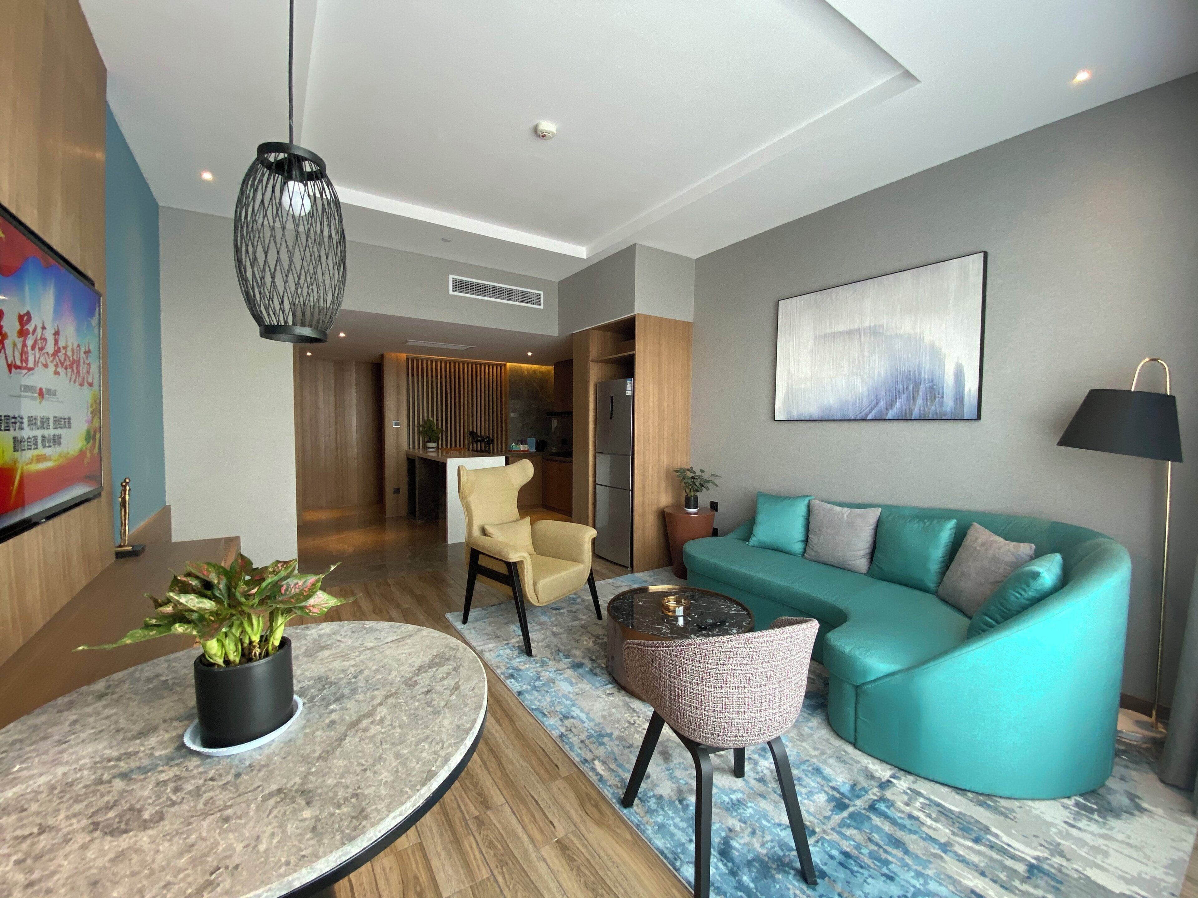 Una sala de estar moderna con un sofá verde azulado, una mesa de centro redonda y una silla. Hay un cuadro en la pared y una planta en maceta sobre la mesa.