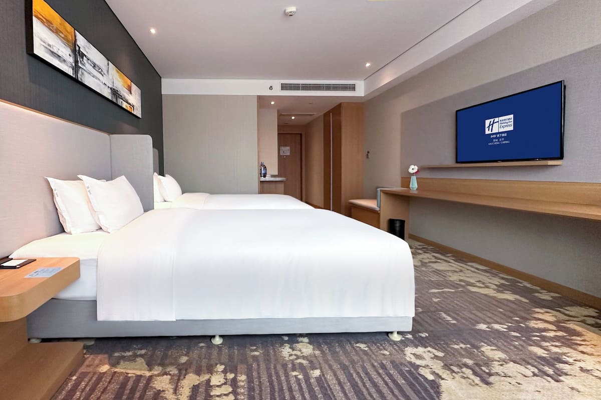 A hotel room with two beds, a flat-screen TV, a bedside table with a tissue box, and a wall-mounted artwork.