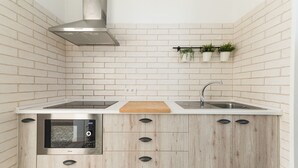 Une cuisine compacte dotée d’un four encastré, d’une hotte en acier inoxydable, d’un évier à deux bacs et de meubles de rangement en bois.