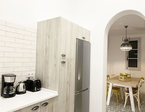 A compact kitchen with a white brick wall, a stainless steel refrigerator, a coffee maker, and a toaster.