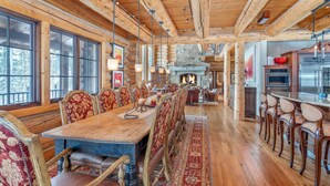 A log cabin interior with a long dining table, chairs, a fireplace, and a kitchen area. - Hilltop Hideaway - Expansive Views From This Private Estate, Hot Tub, Pool Table (Telluride)