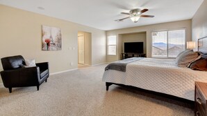 A bedroom with a bed, a black leather chair, a ceiling fan, a TV, and a window with blinds. - Pool/Spa-15 min from ✈️ & strip. Smart TVs Close to shopping 🍔 freeway... (Henderson)