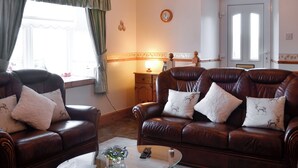 A living room with two leather sofas, a glass coffee table, and a window with curtains. - 4 bedroom accommodation in Fenwick, near Kilmarnock (Fenwick, near Kilmarnock)