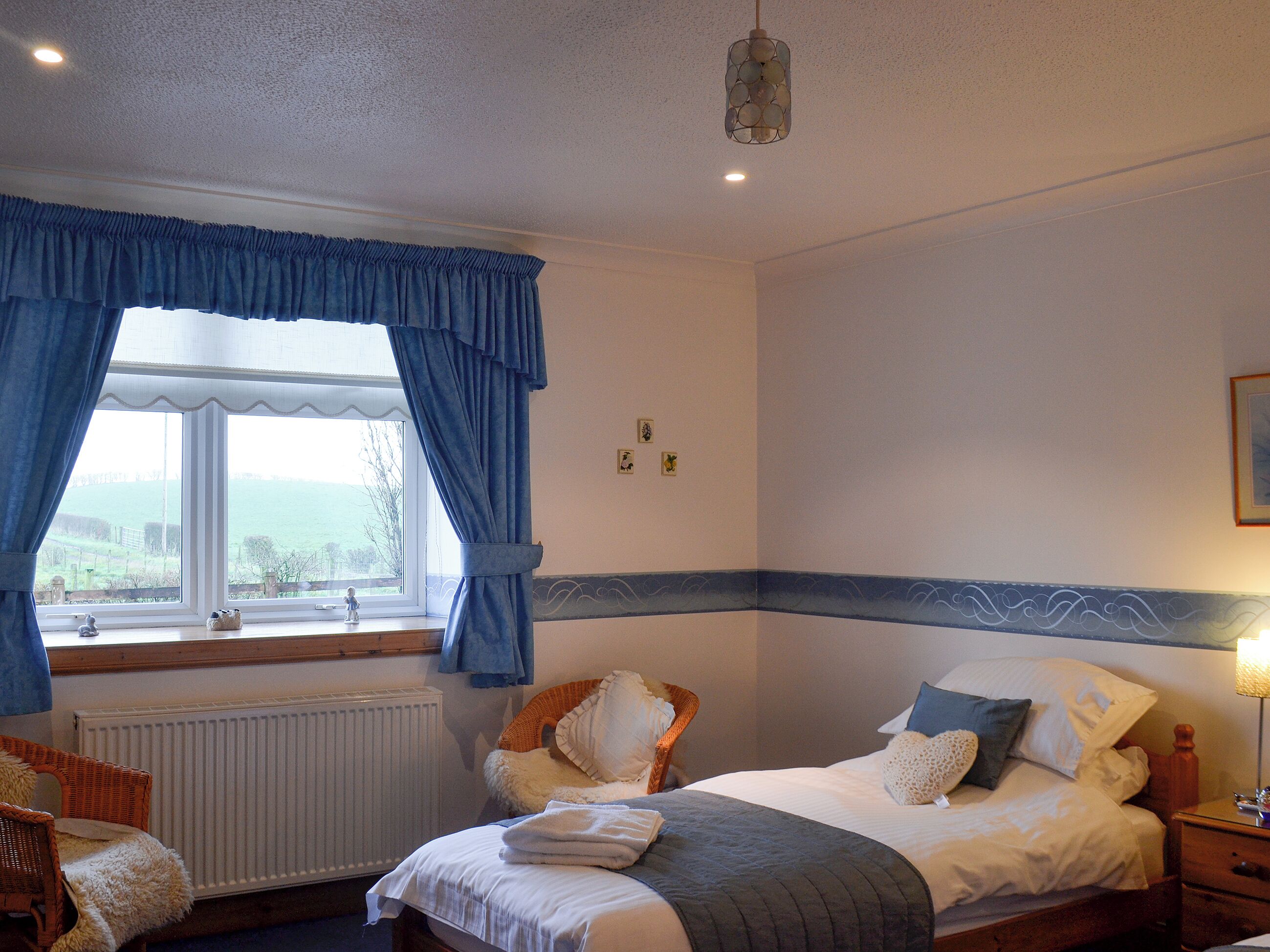 A bedroom with a bed, a window with curtains, a radiator, a chair, and a lamp.