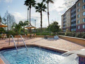 A swimming pool with a water feature, surrounded by palm trees and outdoor seating.