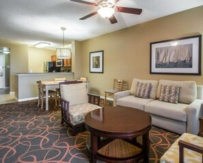 A hotel room with a dining area, a sofa set, a round table, and a ceiling fan.