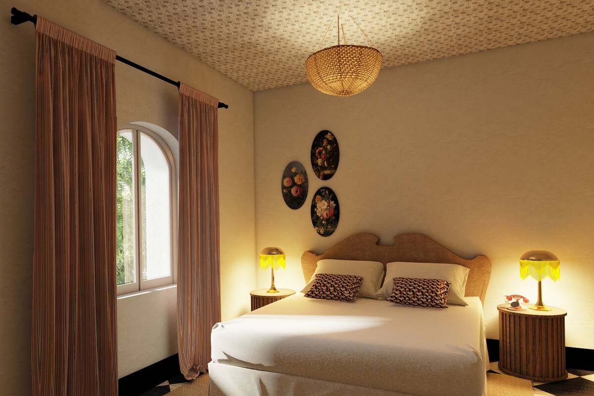 A bedroom with a bed, two bedside tables with lamps, a hanging light fixture, a window with curtains, and wall art.