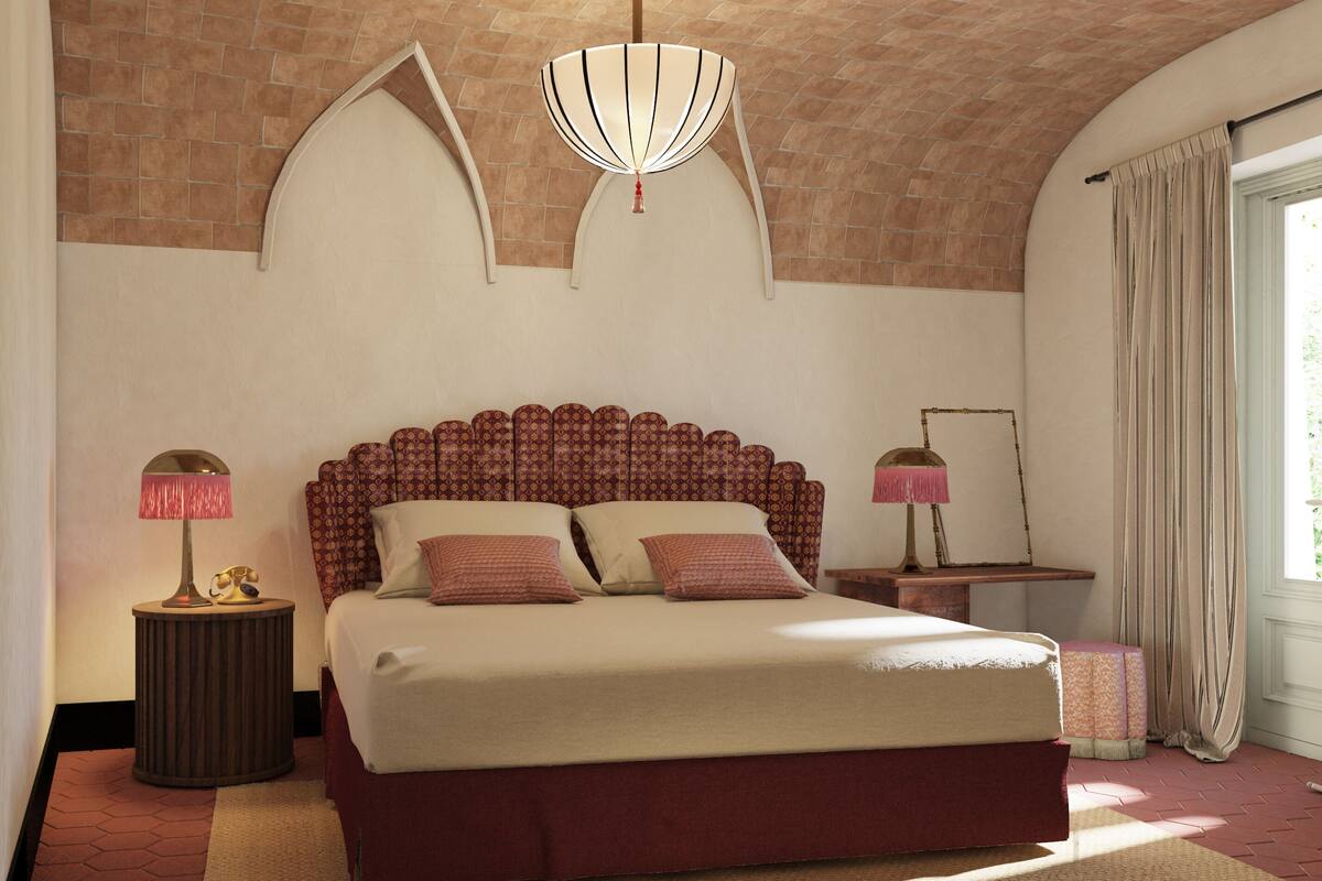 A bedroom with a large bed, two bedside tables, a hanging light fixture, and a window with curtains.