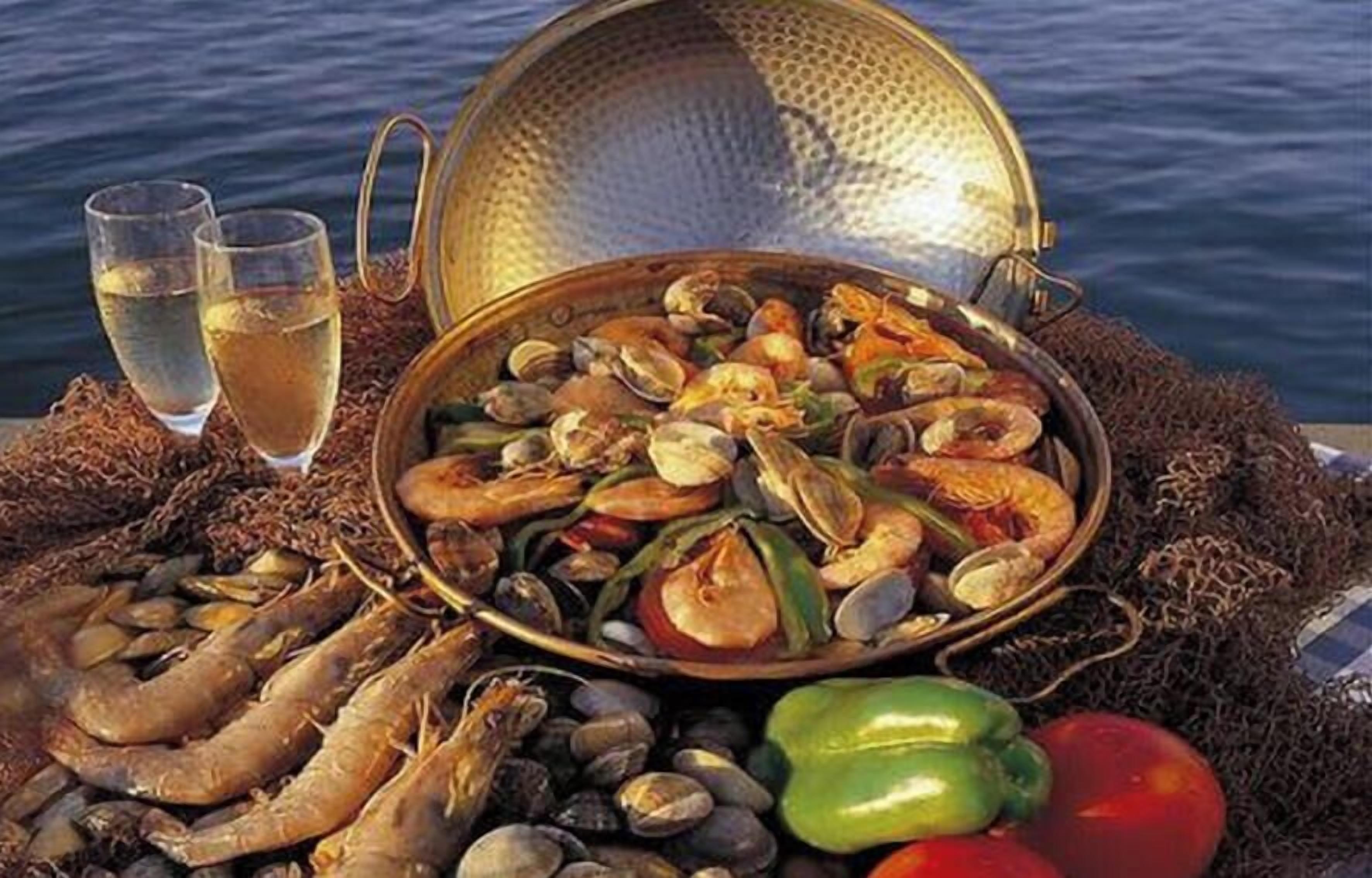 Un plat de fruits de mer composé de palourdes, de crevettes et de légumes, servi sur une table offrant une vue sur la mer.