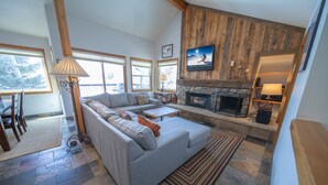 A spacious living room with a stone fireplace, a large gray sofa, and a television mounted on the wall. - Quicksilver 1626 (Keystone)