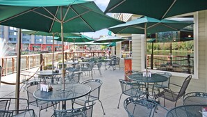 An outdoor patio area with round tables and chairs, green umbrellas, and a view of a body of water. - Decatur 1782 (Keystone)