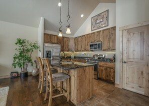 A kitchen with wooden cabinets, stainless steel appliances, a central island with bar stools, and a hanging light fixture. - Frey Gulch 58 (Keystone)