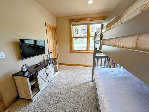 A bunk bed room with a TV, wooden cabinet, and a window. - Frey Gulch 58 (Keystone)