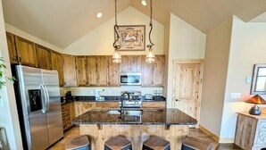 Una cocina con armarios de madera, un refrigerador de acero inoxidable, una isla central con taburetes e iluminación colgante.