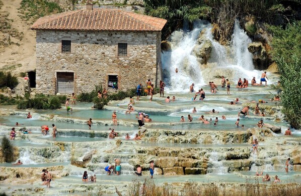A stone building with a tiled roof, surrounded by terraced pools and a waterfall. - La Rosa Canina [Tuscany cottage] (Cana)