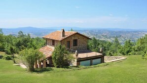 A stone house with a tiled roof, surrounded by a grassy landscape and trees, overlooking a valley. - La Rosa Canina [Tuscany cottage] (Cana)