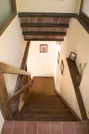 A wooden staircase with a handrail, leading to a landing with a framed picture and a vase with flowers. - La Rosa Canina [Tuscany cottage] (Cana)