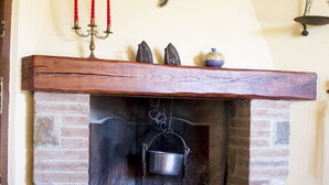 A fireplace with a stone surround, a wooden mantel, and a hanging wreath above it. - La Rosa Canina [Tuscany cottage] (Cana)