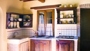 A kitchen with wooden cabinets, a tiled backsplash, a window with curtains, and a gas stove. - La Rosa Canina [Tuscany cottage] (Cana)