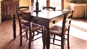 A wooden dining table with four chairs, a wine bottle, and two wine glasses. - La Rosa Canina [Tuscany cottage] (Cana)