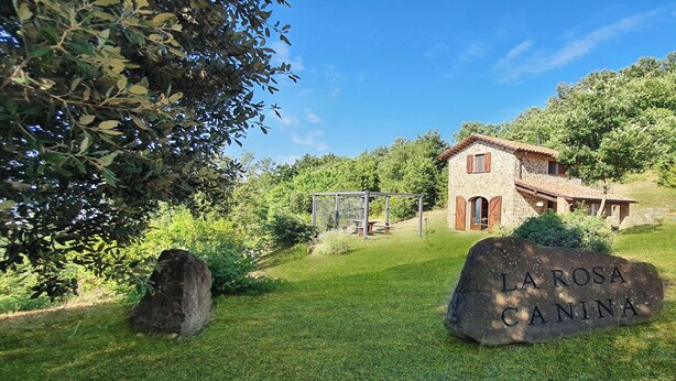 A stone house with a stone roof, surrounded by greenery and a large rock with 'LAROSA CANINA' inscribed. - La Rosa Canina [Tuscany cottage] (Cana)