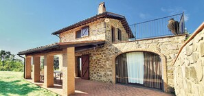 A two-story stone house with a balcony, a covered patio, and a large arched window. - La Rosa Canina [Tuscany cottage] (Cana)