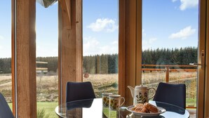 A table with chairs and a view of a forest through large windows. - 3 bedroom accommodation in Glenlivet, near Dufftown (Glenlivet, near Dufftown)