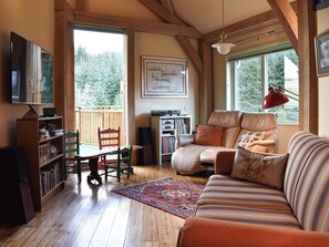 Un accogliente soggiorno con pavimento in legno, un divano, una poltrona, una libreria, un televisore e una finestra con vista sugli alberi.