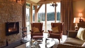 A cozy room with a fireplace, two armchairs, a sofa, a glass coffee table, and a TV mounted on a stone wall. - 3 bedroom accommodation in Glenlivet, near Dufftown (Glenlivet, near Dufftown)