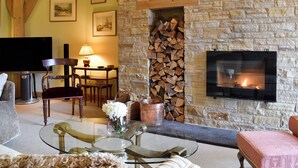 A living room with a stone wall, a fireplace, a television, and a dining area with a table and chairs. - 3 bedroom accommodation in Glenlivet, near Dufftown (Glenlivet, near Dufftown)