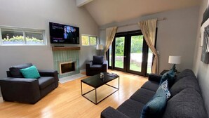 A living room with a fireplace, a television, and a large window with curtains. - Surfrider at the Del Mar Beach Colony (Del Mar)