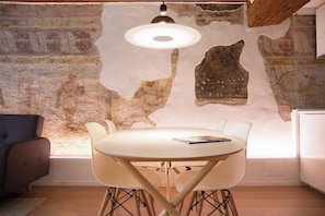 A dining area with a round table and chairs, a modern pendant light, and a wall with exposed brick and a large stone.