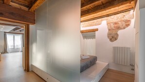 A modern bedroom with a large mirror, wooden ceiling beams, a bed with a headboard, and a radiator.