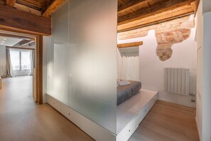 A modern bedroom with a large mirror, wooden ceiling beams, a bed with a headboard, and a radiator.