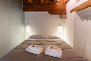 A single bed with a brown quilt, two folded towels, and two wall-mounted light fixtures.