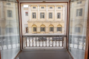 A balcony with a wrought iron railing overlooking a building with arched windows and classical columns.