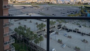 A high-rise building with balconies overlooking a marina, parking area, and a distant bridge. - Ocean Blvd (Long Beach)