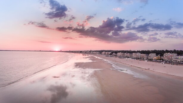 A beach with a sunset, buildings along the shore, and a calm sea. - Charming T1 Bis 50m from the Beach and the Market (Pornichet)