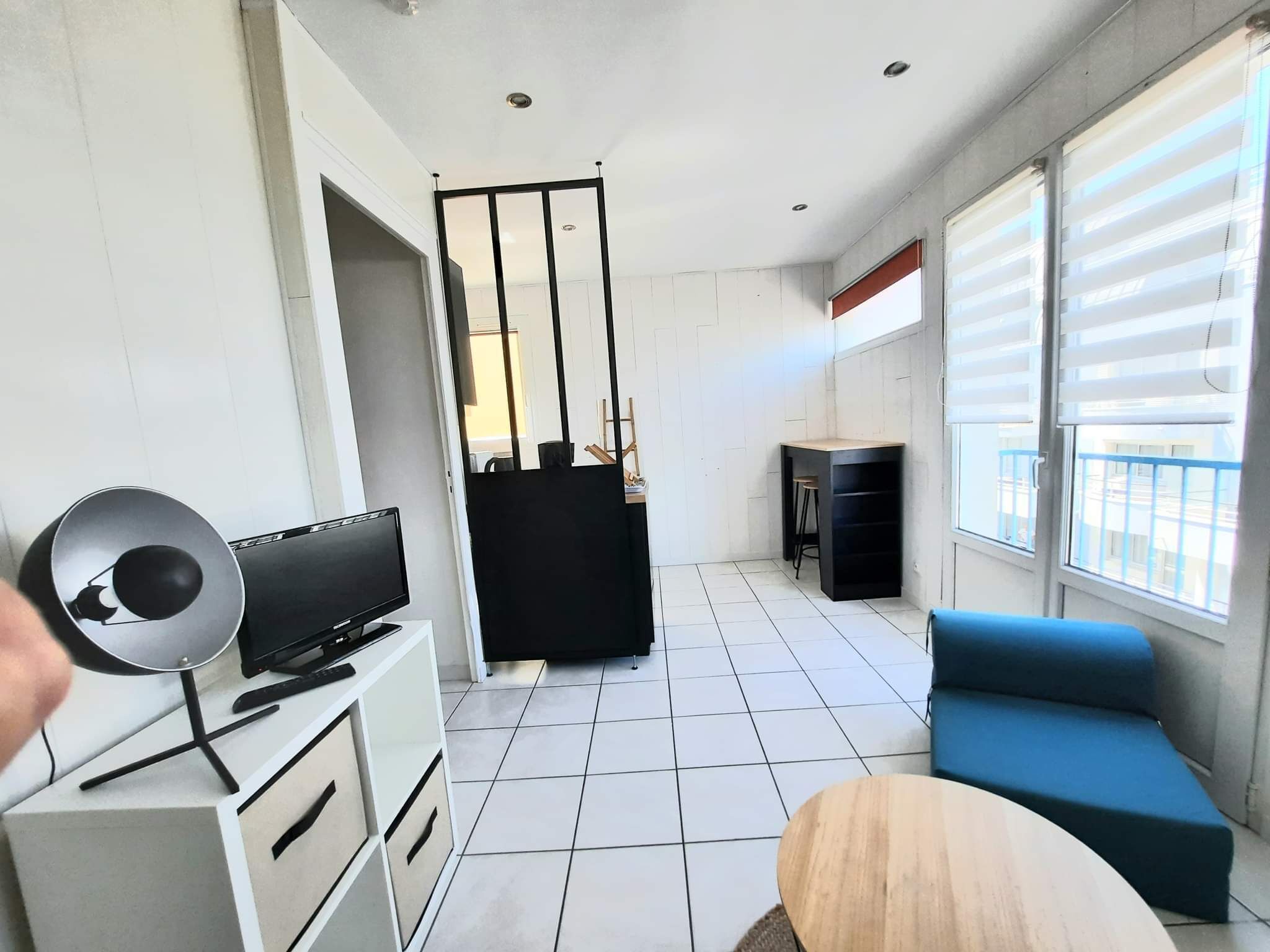 A modern living room with a TV, a blue sofa, a small wooden table, and a balcony with a view.