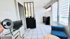A modern living room with a TV, a blue sofa, a small wooden table, and a balcony with a view. - Charming T1 Bis 50m from the Beach and the Market (Pornichet)