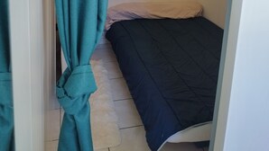 A small, narrow room with a bed against the wall, a curtain tied at the top, and a framed picture on the wall. - Charming T1 Bis 50m from the Beach and the Market (Pornichet)
