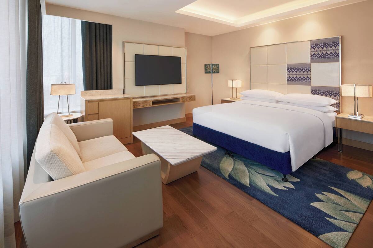 A modern hotel room with a bed, a sofa, a TV, and a desk.